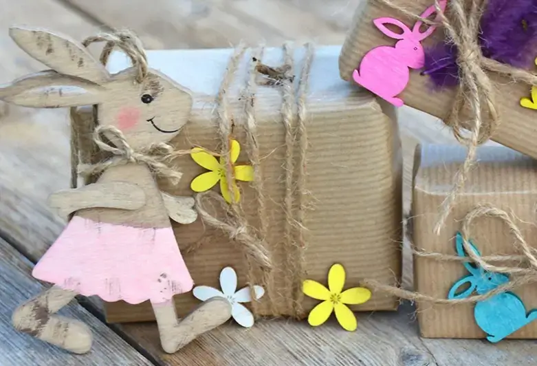 Gifts wrapped in brown kraft paper with jute cord, colorful bunny tags and wooden bunny figurine on wooden table.