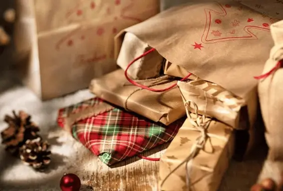 Weihnachtlich verpackte Geschenke in braunem Kraftpapier und rotem Karostoff, dekoriert mit roter Kordel, Tannenzapfen und Christbaumkugeln.