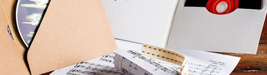 Schallplattenhülle, CD und Notenblatt neben einer weißen Verpackung auf Holzuntergrund.