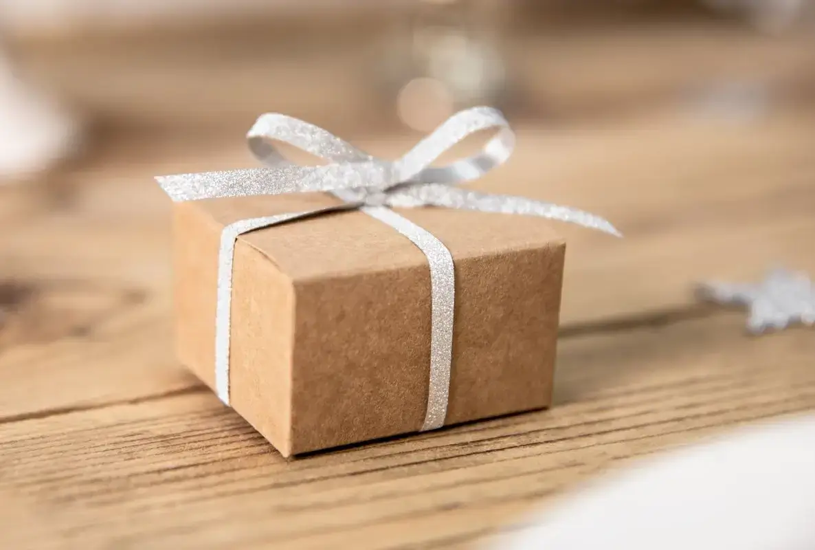Kleine braune Geschenkbox aus Kraftkarton mit silbernem Band auf Holzoberfläche.