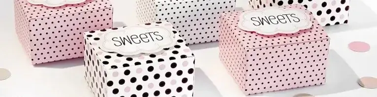 Petites boîtes-cadeaux roses et blanches, parsemées de pois noirs et ornées d'étiquettes portant l'inscription « Sweets ».