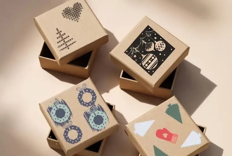 Vier kleine Geschenkschachteln aus braunem Karton mit weihnachtlichen Motiven wie Tannenbäumen, Christbaumkugeln, Kränzen, Herz und Handschuh.